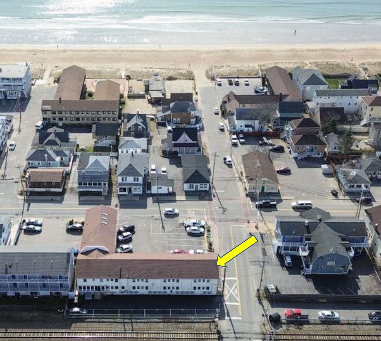 Vue aérienne d’une zone résidentielle côtière, avec des maisons, une gare et une plage en arrière-plan.