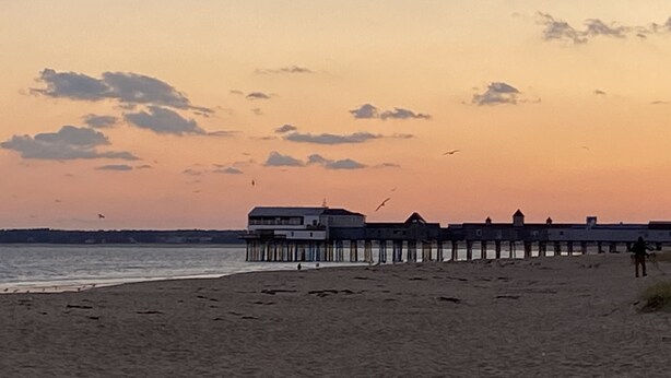 A beach with a pier extending into the water, featuring a building with multiple levels. - Oceanview! Cozy Condo with Kitchen, Living Area, Porch, 2 Reserved Parking Spots (Old Orchard Beach)