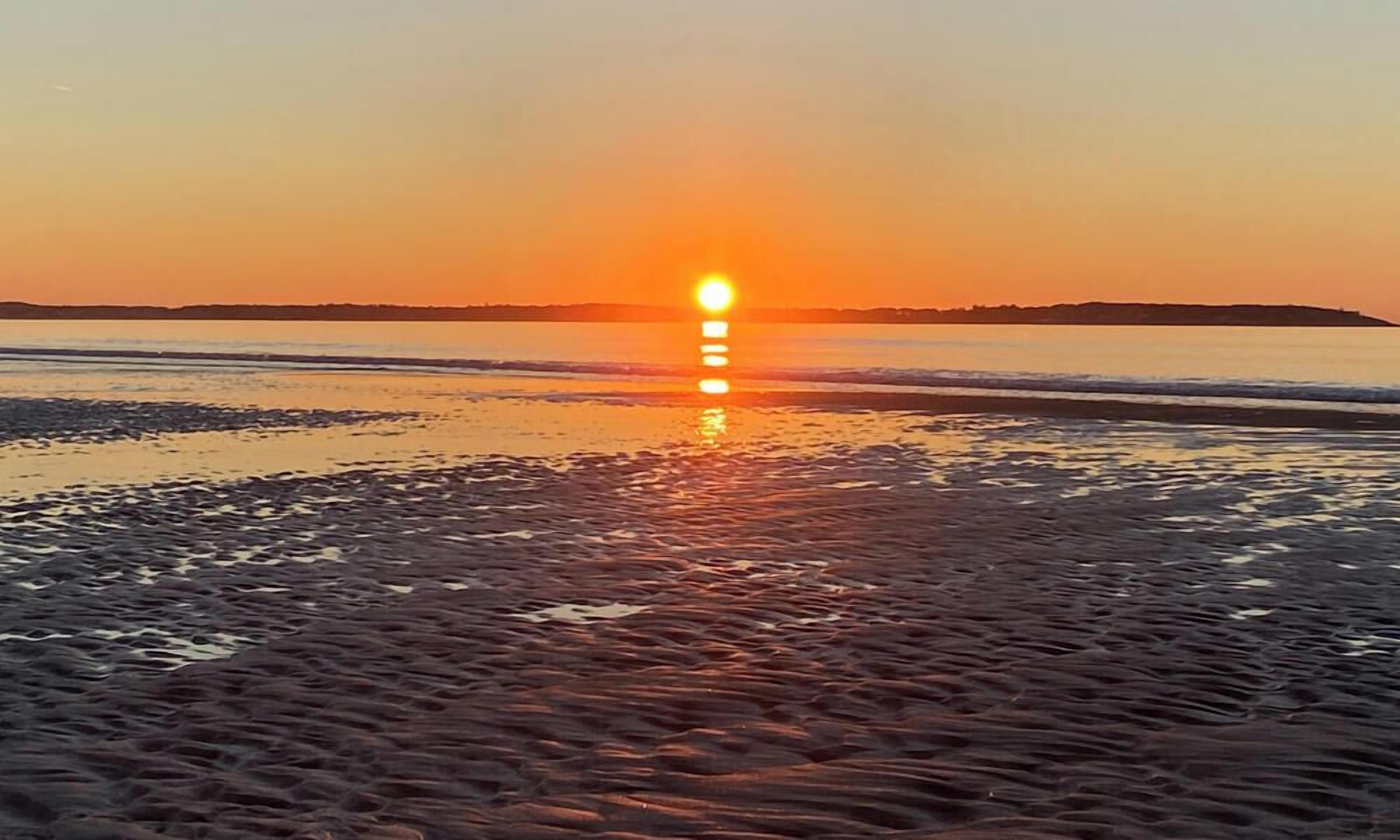 Een strand met de ondergaande zon aan de horizon, weerkaatsend op het water.
