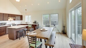 Una cocina amplia con suelo de madera, una isla central con taburetes y ventanas grandes que dejan entrar luz natural.