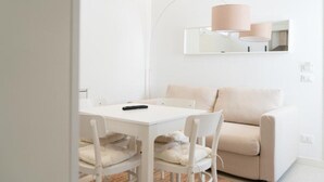 A minimalist room with a white table, two white chairs, a beige sofa, and a single lamp. - Maruzza Home 103 (Favignana)