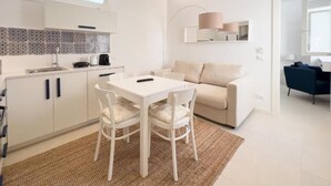 A modern, well-lit kitchen with white cabinets, a tiled backsplash, and a dining area with a white table and chairs. - Maruzza Home 103 (Favignana)