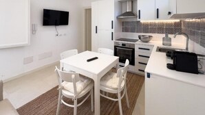 A modern kitchen with white cabinetry, a built-in oven, and a microwave. There is a dining table with chairs and a TV mounted on the wall. - Maruzza Home 103 (Favignana)