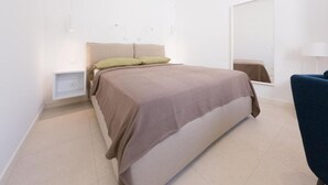 A bedroom with a bed, bedside tables, a mirror, and a chair. - Maruzza Home 103 (Favignana)