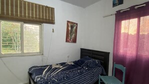 Pequeña habitación individual con ventana, una silla y una cama con colcha estampada.