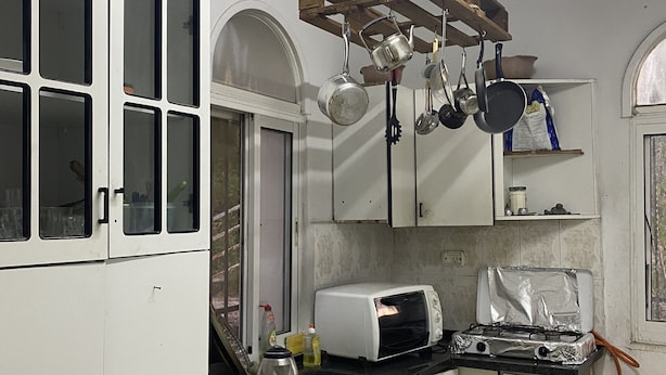 Una cocina compacta con muebles blancos, un tostador, una estufa a gas y ollas colgantes.