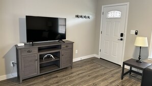 A room with a TV on a wooden cabinet, a door with a window, and a small table with a lamp.