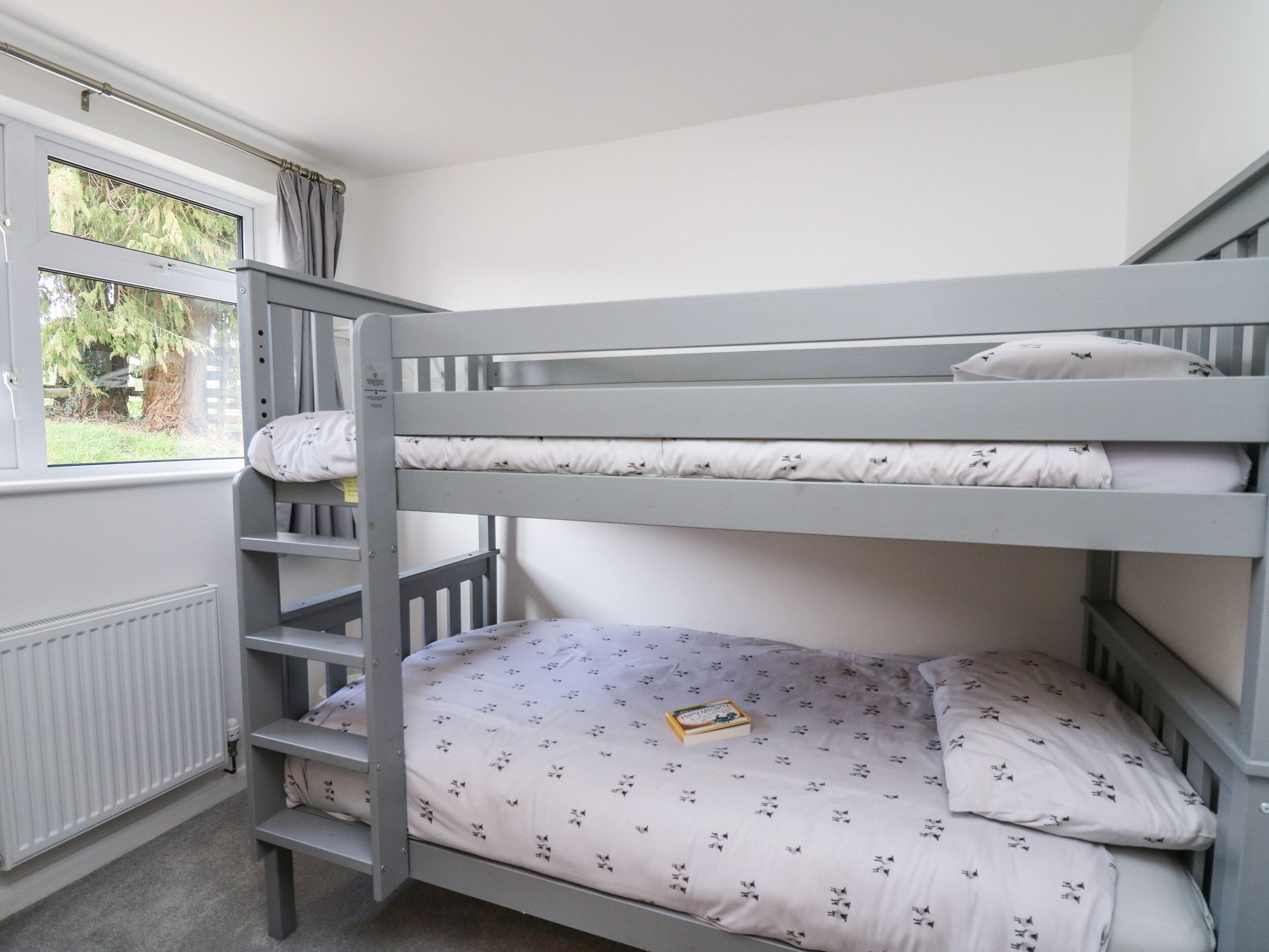 A bunk bed with a window, a radiator, and a book on the lower bunk.