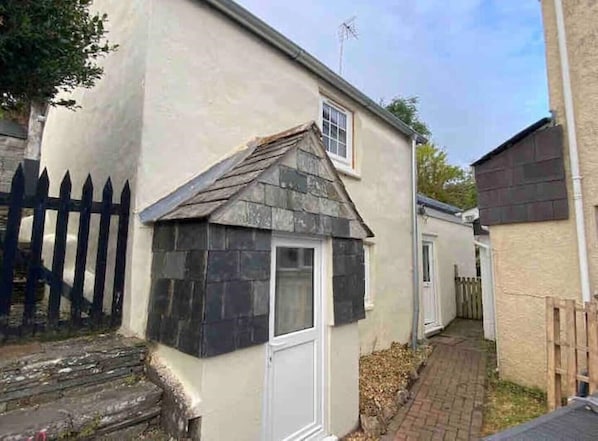 Une petite maison à un seul étage, avec un toit en pente, une porte d’entrée et une cheminée bien visible.