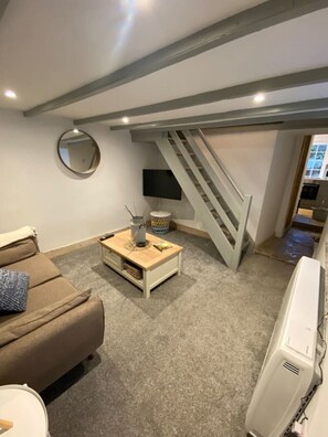 Un salon comprenant un canapé, une table basse, un téléviseur et un escalier menant à l’étage supérieur.