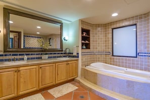 Un baño con un espejo grande, un lavabo con dispensador de jabón, una bañera y un estante con artículos de aseo.