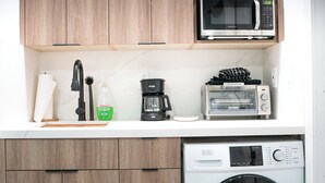 Uma cozinha compacta com armários de madeira, micro-ondas, cafeteira, torradeira e máquina de lavar roupa.