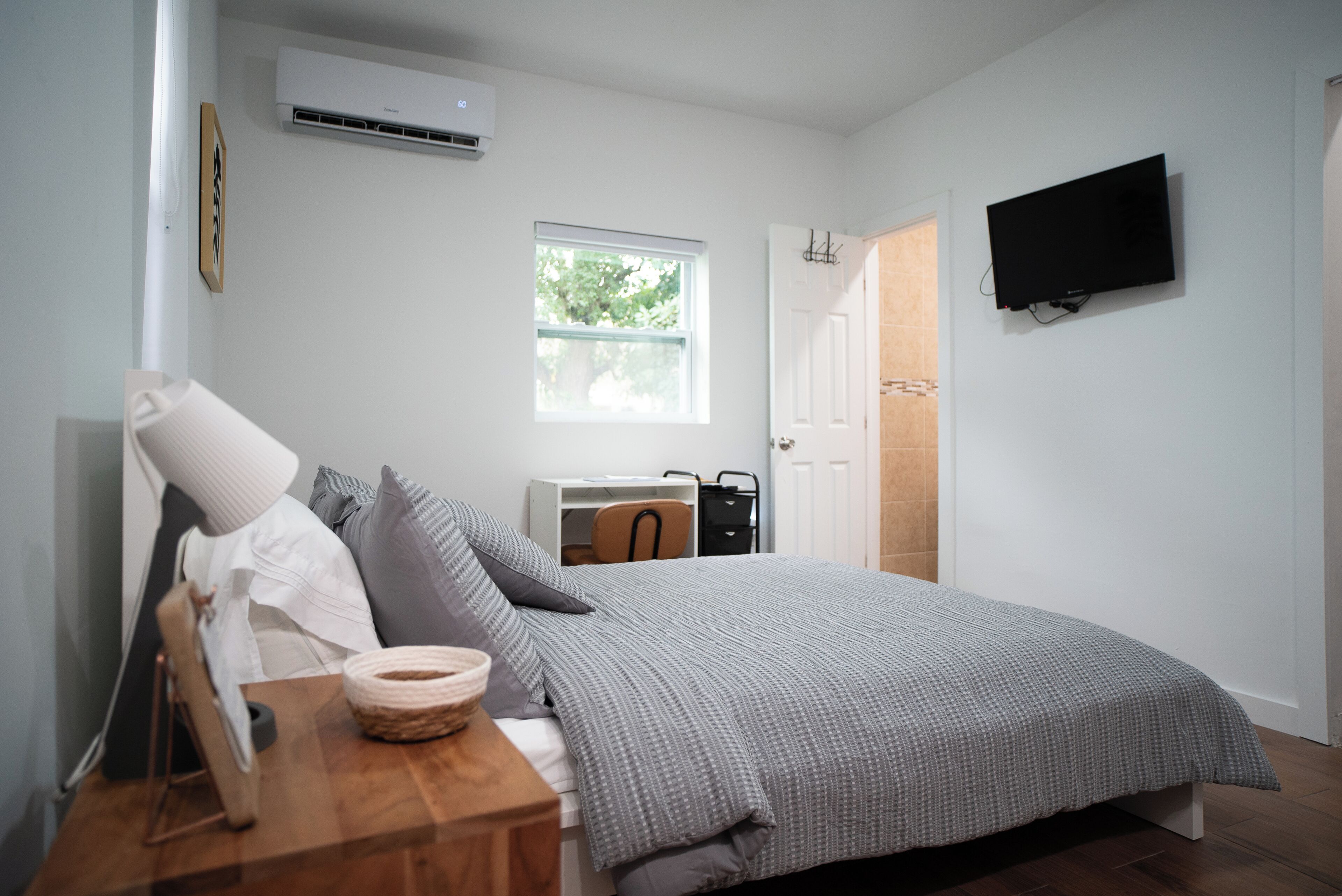 A bedroom with a bed, a desk, a chair, a TV, and a window.