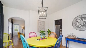 A dining area with a yellow table, colorful chairs, a hanging light fixture, and a decorative wall piece. - Colorful, waterside home (Bradenton)