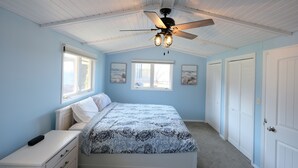 Un dormitorio con una cama, una mesita de noche, un ventilador de techo y una ventana.