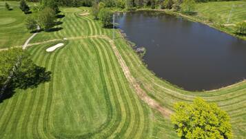 A golf course with a pond, surrounded by trees and a building in the distance.