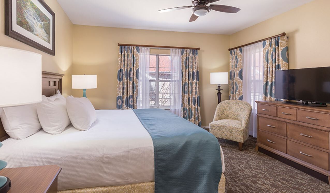 A hotel room with a bed, two bedside lamps, a television, a chair, and a dresser.
