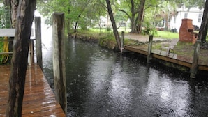 A wooden dock extending over a calm river, surrounded by lush greenery and a brick structure on the right. - Scallop Hut - Old Homosassa (Homosassa)
