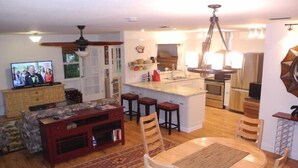 A modern kitchen with an island, a dining area with a table and chairs, a TV in the living room, and a ceiling fan. - Scallop Hut - Old Homosassa (Homosassa)
