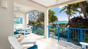 A balcony with a view of the ocean, white furniture, and a ceiling fan.
