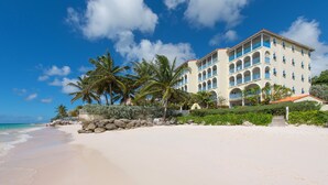 A beachfront hotel with multiple balconies, a sandy beach, and palm trees.
