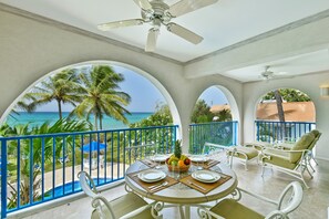 Un balcon avec vue sur l’océan, aménagé avec des chaises et une table dressée pour les repas.
