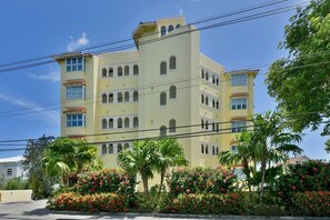 Un hôtel à plusieurs étages, doté d’une façade jaune pâle, de nombreux balcons et d’un jardin agrémenté de fleurs rouges.
