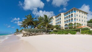 Ein Hotel direkt am Strand mit heller Fassade, blauen Balkonen und blauem Himmel.