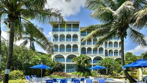 A hotel with a pool area, blue umbrellas, and lounge chairs.
