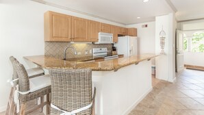 A kitchen with wooden cabinets, a microwave, an oven, and a sink. There are wicker chairs and a bar counter.