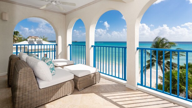A balcony with a wicker sofa, a ceiling fan, and a view of the ocean.