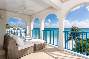 Un balcon avec un canapé en osier, un ventilateur de plafond et une vue sur l’océan.