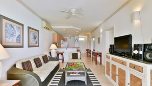 A living room with a sofa, coffee table, and TV. There is a kitchen in the background.