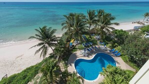 Un complexe hôtelier doté d’une piscine entourée de palmiers et de chaises de plage, offrant une vue sur la plage et l’océan.