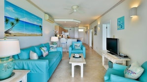 Een moderne woonkamer met turquoise banken, een televisie en kunstwerken die een strandscène voorstellen.