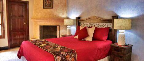 A bedroom with a large bed, two bedside lamps, a fireplace, and a door.