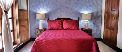 Un dormitorio con una cama grande, dos mesitas de noche con lámparas, un armario de madera y una ventana con cortinas.