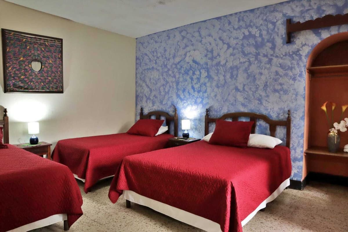 Habitació d'hotel amb dos llits individuals, una tauleta de nit amb una làmpada, una obra d'art penjada a la paret i una estant decorativa amb flors.