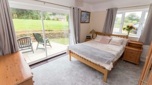 Une chambre à coucher comprenant un lit, une table de chevet, une commode en bois et une porte-fenêtre coulissante donnant sur une terrasse avec une chaise.