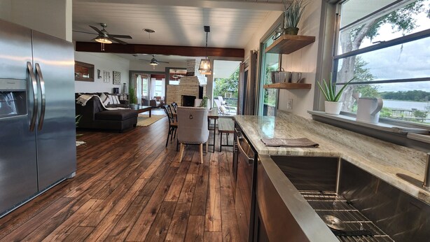 Una cocina moderna con un refrigerador de acero inoxidable, pisos de madera y un amplio ventanal con vista a un lago.