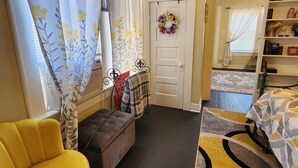 A cozy room with a yellow armchair, a bench, a patterned rug, and a door with a floral wreath. - Adorable & Romantic French Corner by Downtown, The Heights & WOMH - Pet Friendly (Houston)