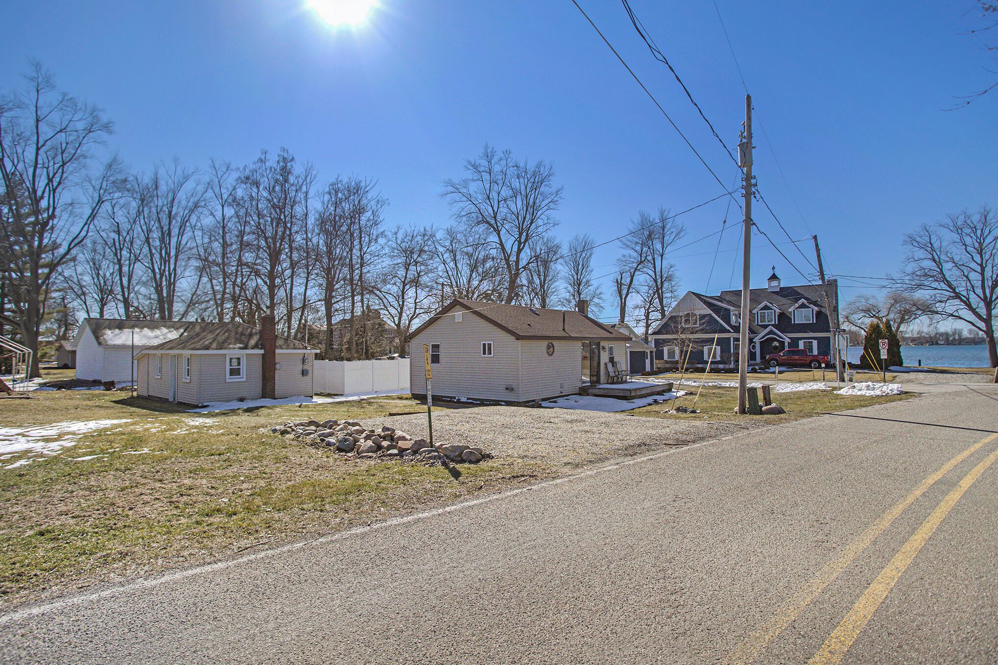 A residential area with houses, a gravel road, and a body of water in the background.