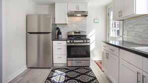 A compact kitchen with white cabinets, stainless steel appliances, and a patterned rug. - Beautiful 2 bed cottage by Coldwater Lake! (Coldwater)