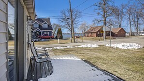 A residential area with a house, a parked red vehicle, and a body of water in the background. - Beautiful 2 bed cottage by Coldwater Lake! (Coldwater)