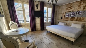 Una habitación con una cama, una mesa con una silla, un televisor y una pared de piedra.
