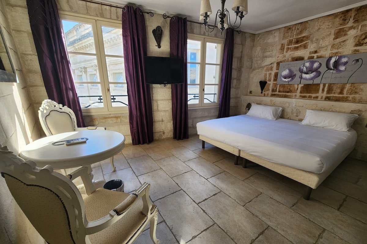 Una habitación con una cama, una mesa con una silla, un televisor y una pared de piedra.