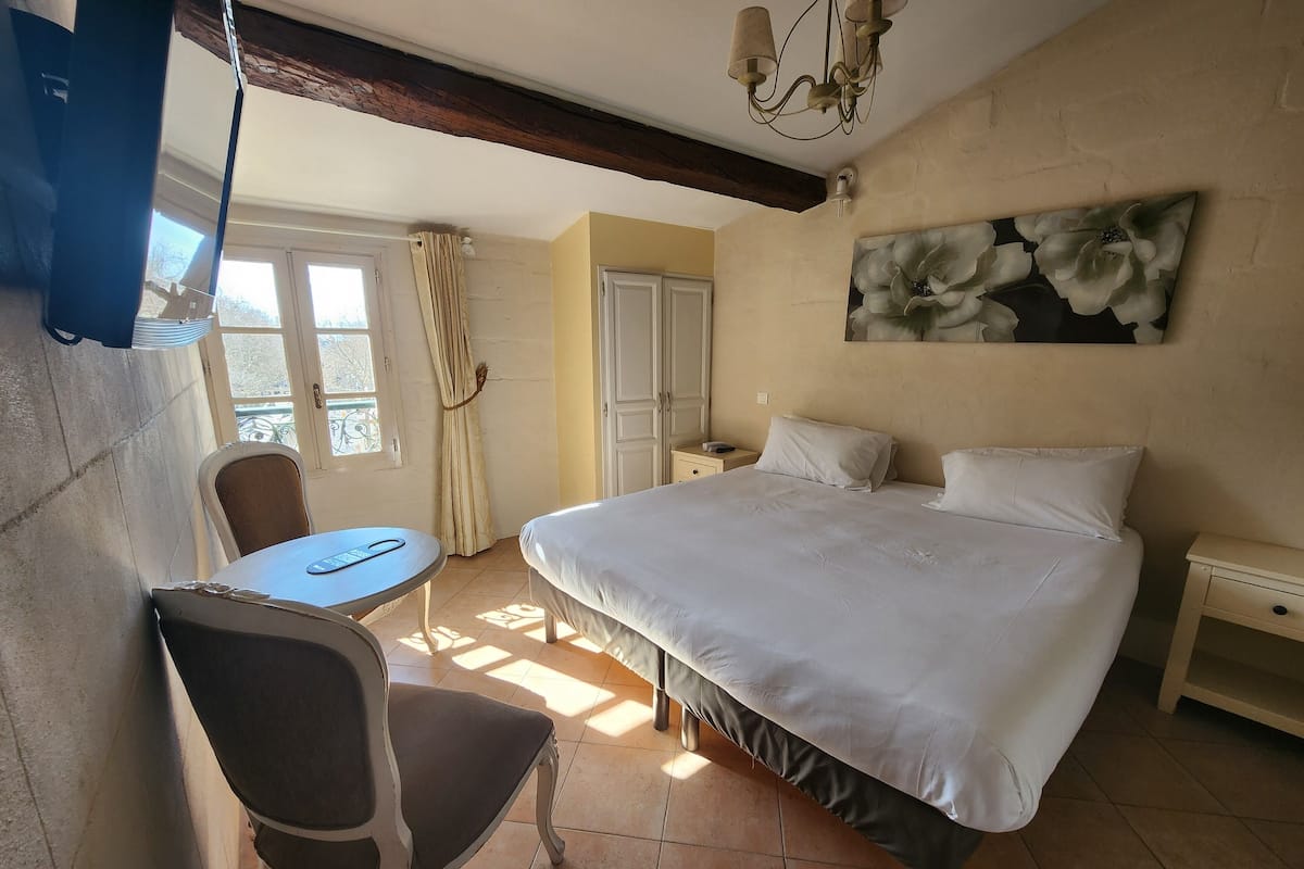 Un dormitorio con una cama grande, una silla, una mesita y un cuadro en la pared.
