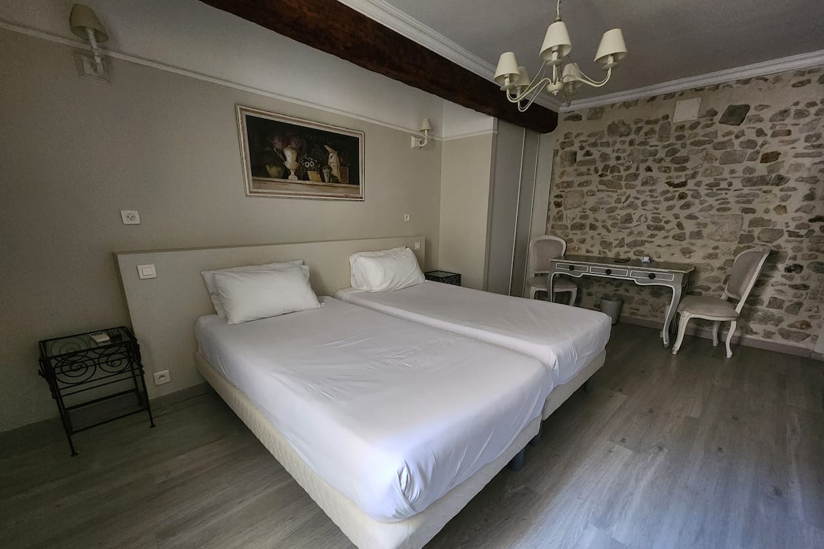 Cama doble con sábanas blancas, un escritorio con silla y una pared de piedra.