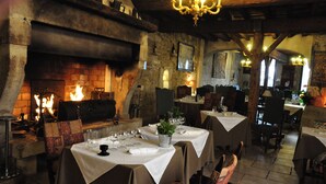A rustic dining area with tables set for two, a fireplace, and exposed wooden beams. - Hôtel du Palais des Papes (Avignon)