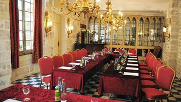 A banquet hall with long tables, red velvet tablecloths, gold chandeliers, and red upholstered chairs.